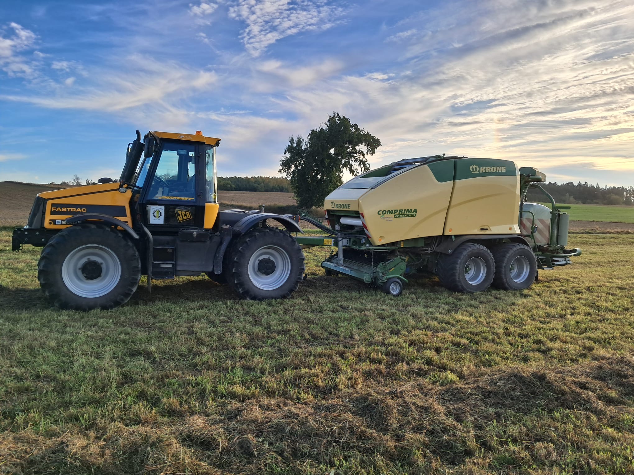 JCB Fastrac mit Krone-Comprima-Rundballenpresse seitlich im Abendlicht