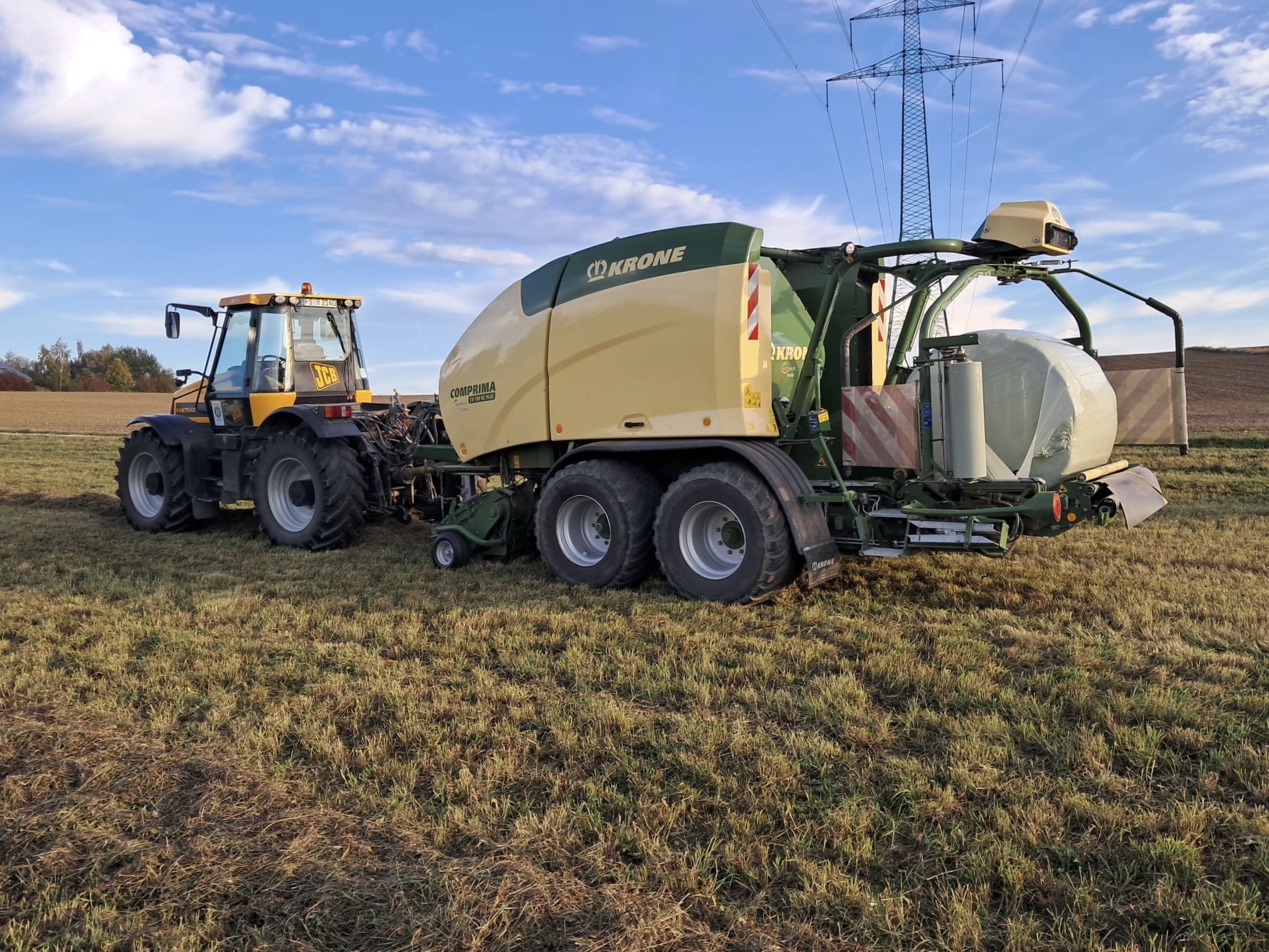 JCB Fastrac mit Krone-Comprima-Rundballenpresse und gewickeltem Ballen auf der Wiese