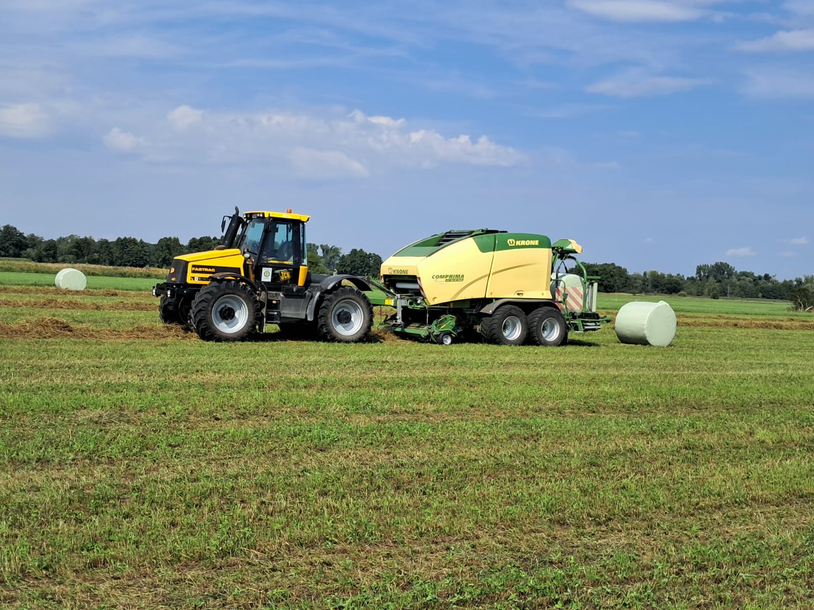 JCB Fastrac mit Krone-Rundballenpresse bei der Arbeit, daneben fertige Silageballen